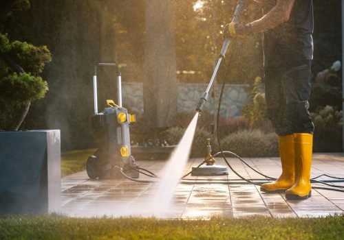 A Person Power Washing a Patio With a Pressure Washer in a Sunny Outdoor Setting